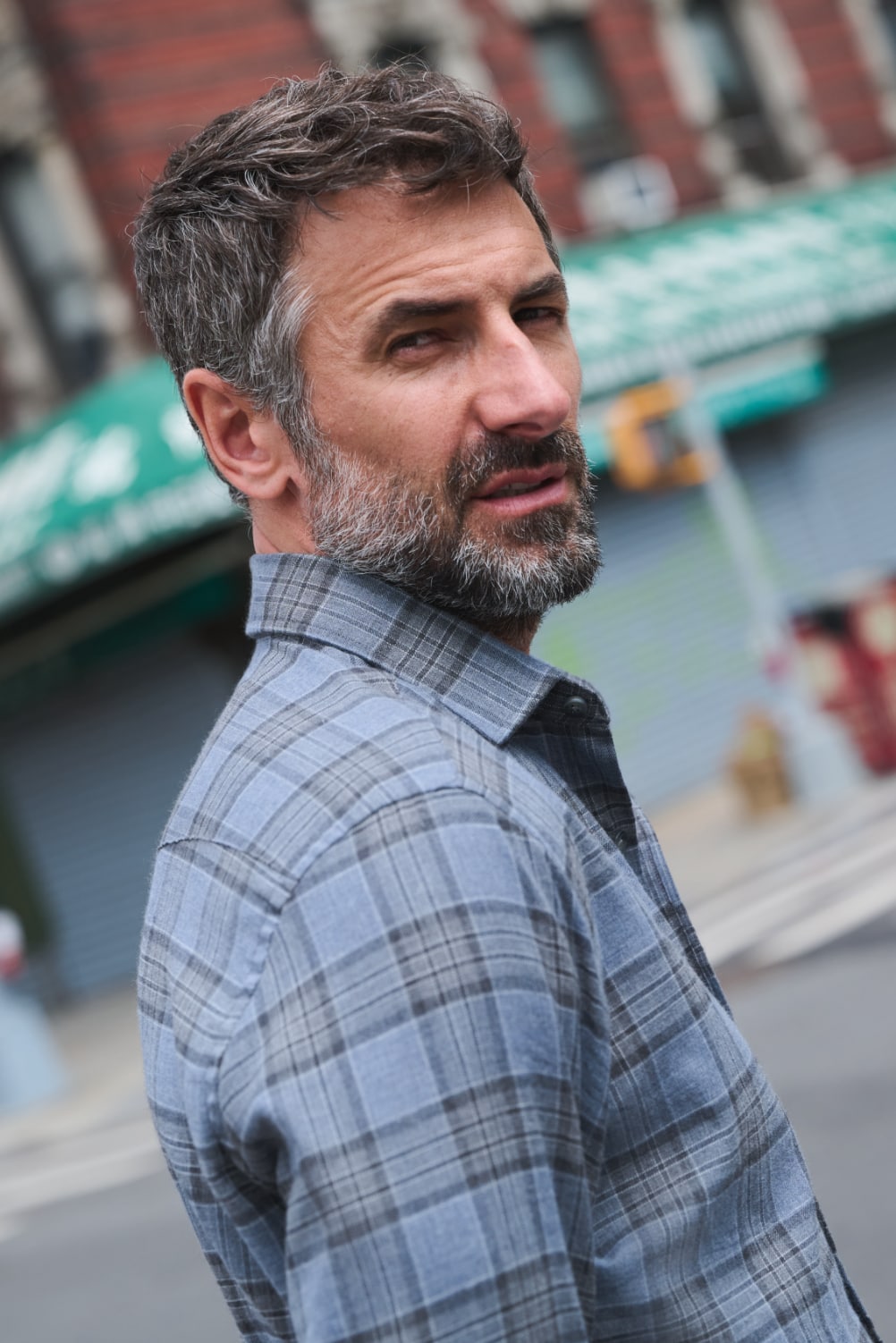 Man wearing plaid shirt with hands in pockets on crosswalk