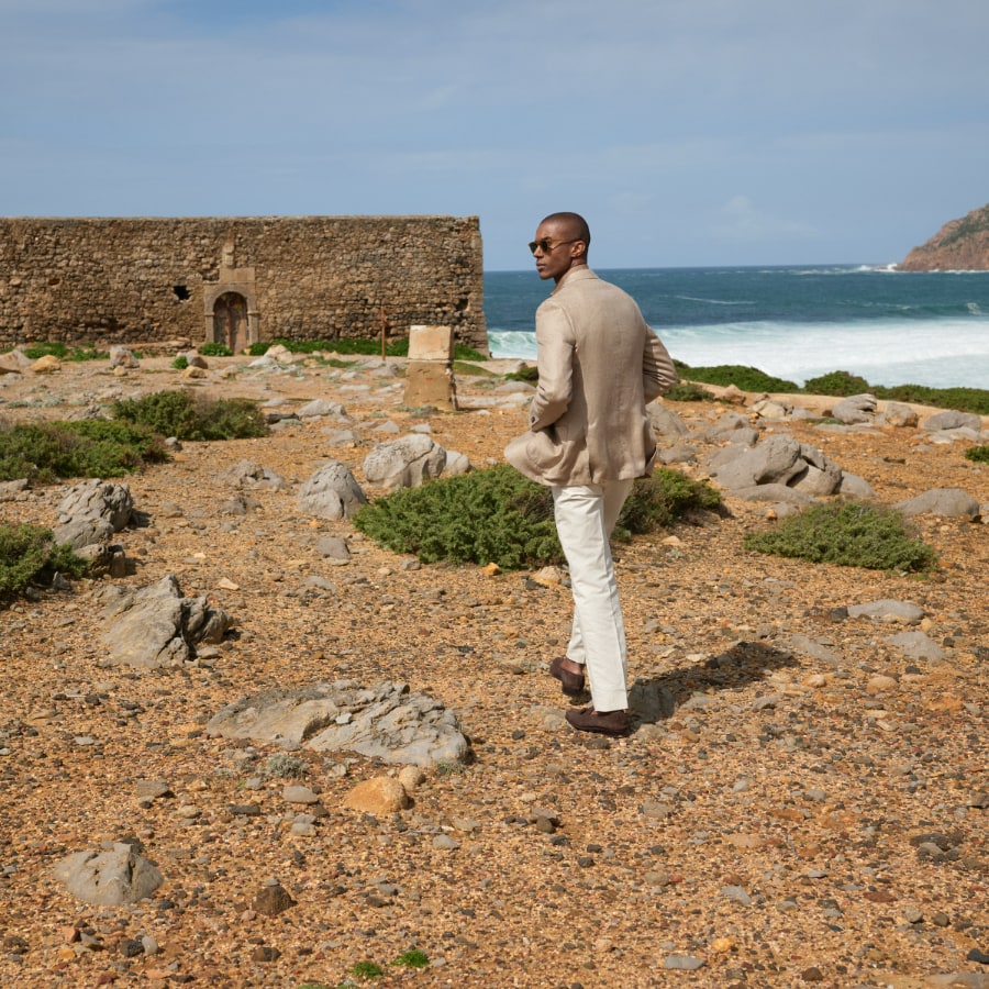 Man wearing a jacket and knit shirt, standing on a rocky beach