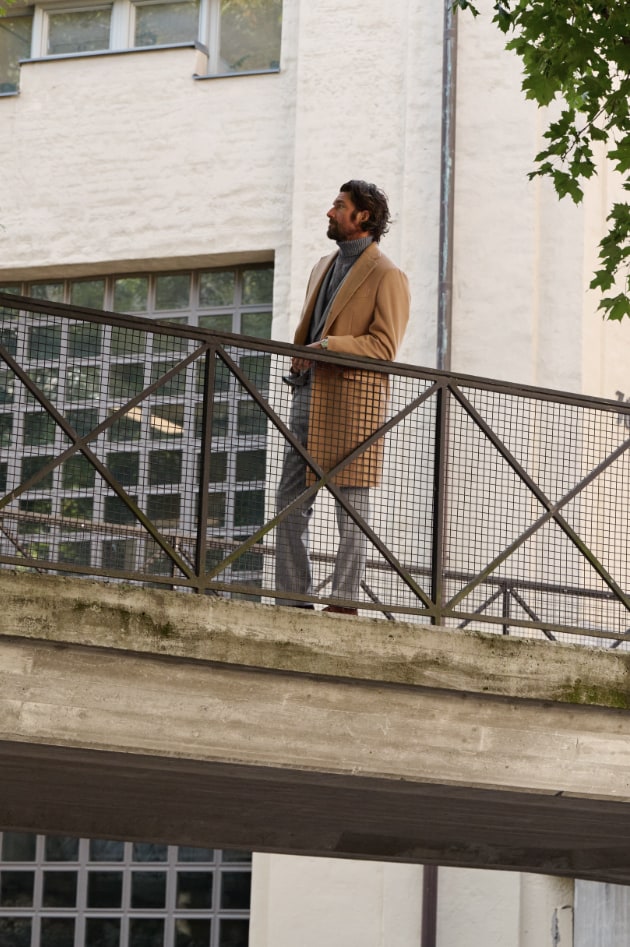 Man wearing flannel overcoat, standing on a foot bridge